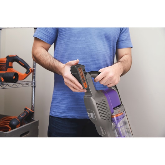 Photo d'une personne tenant un aspirateur sans fil BLACK+DECKER BHFEV182CP avec batterie amovible 18V visible.