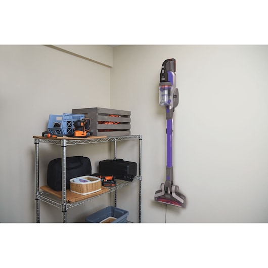 Aspirateur balai sans fil BLACKDECKER BHFEV182CP monté au mur dans une pièce de rangement à côté d’une étagère métallique avec des outils.