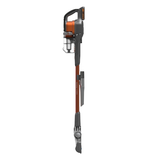 Een snoerloze steelstofzuiger met oranje en zwarte accenten, een transparante stofcontainer en een bevestigd mondstukaccessoire, afgebeeld in verticale positie tegen een witte achtergrond.