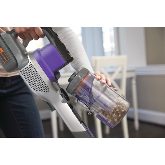 Photo de l’aspirateur sans fil BLACKDECKER BHFEV362DP avec des accents violets, vidage du bac à poussière en intérieur.