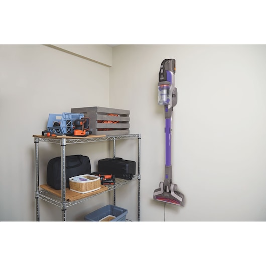 Aspirateur balai sans fil BLACKDECKER BHFEV362DP fixé au mur dans une buanderie près d'une étagère métallique avec outils.