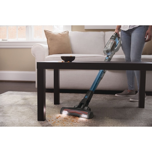 BLACKDECKER BHFEV362D aspirateur balai sans fil nettoyant des miettes sous une table basse dans un salon.