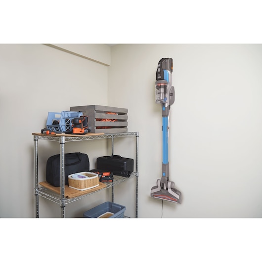 Aspirateur balai sans fil BLACKDECKER BHFEV362D monté au mur dans une pièce de rangement à côté d'étagères métalliques.
