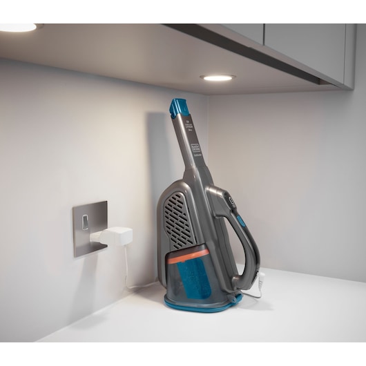 Foto van de BLACKDECKER BHHV320J handstofzuiger die oplaadt op een wit aanrecht onder een kast.