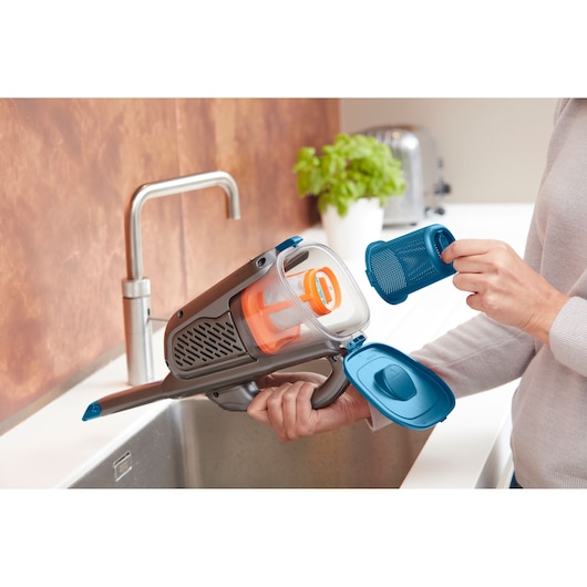 BLACKDECKER BHHV320J handstofzuiger met open stofreservoir voor reiniging boven een keukengootsteen.