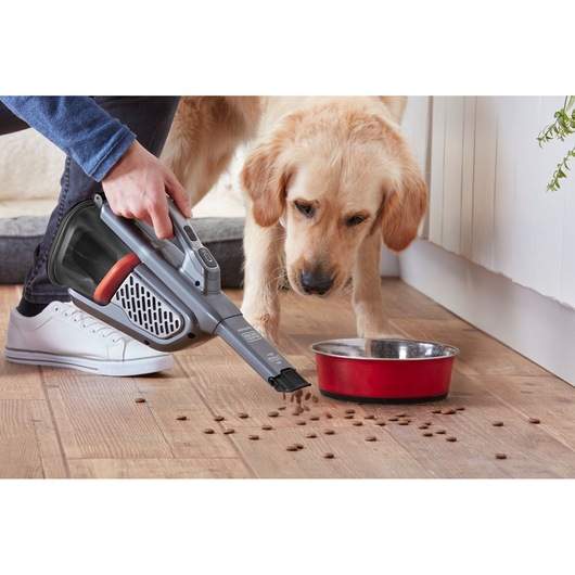 BLACKDECKER BHHV520JF aspirateur à main nettoyant des croquettes près d’un bol rouge sur sol en bois, scène intérieure.