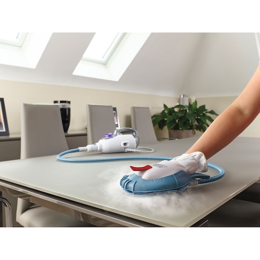BLACKDECKER BHSM1615DSM handstoomreiniger reinigt tafelblad, close-up, wit-blauw apparaat met mesh handschoen.
