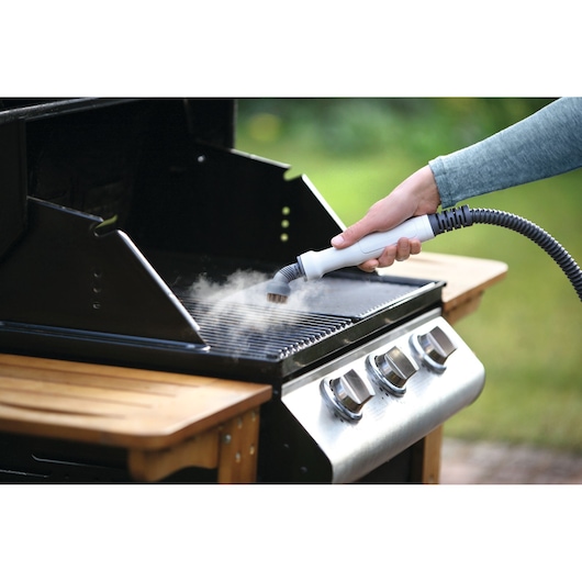 Foto van BLACKDECKER BHSM1615DSM handstoomreiniger die wordt gebruikt om een buitenbarbecue schoon te maken.