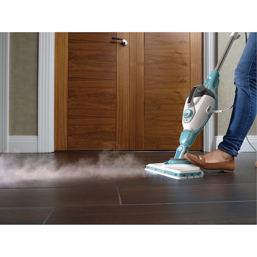 BLACKDECKER BHSM168DSM stoomreiniger op donkere tegelvloer, persoon drukt op pedaal, stoom zichtbaar.