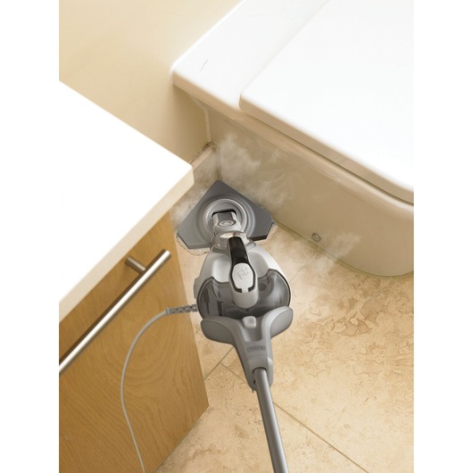 Een BLACK+DECKER stoommop reinigt een betegelde vloer naast een badkamerkast en toilet, met zichtbaar stoom dat uit de mopkop komt.
