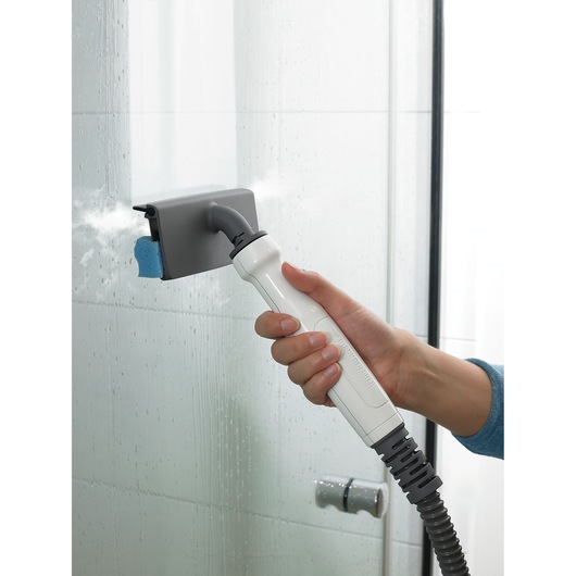 Een persoon gebruikt een BLACK+DECKER handstoomreiniger om een glazen douchedeur schoon te maken, met zichtbare stoom en waterdruppels.