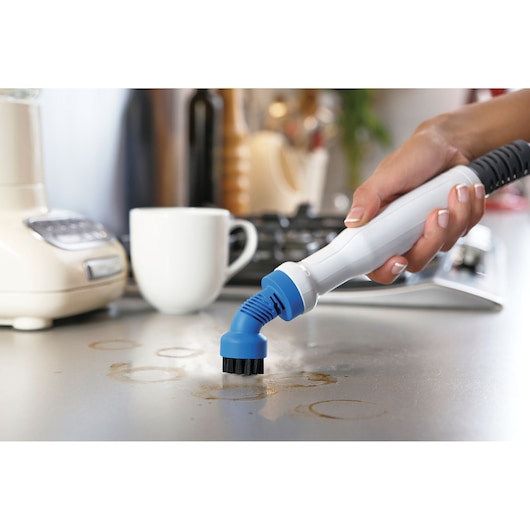 Foto van BLACKDECKER BHSM168U stoomreiniger met handborstel die een aanrecht met koffievlekken schoonmaakt.