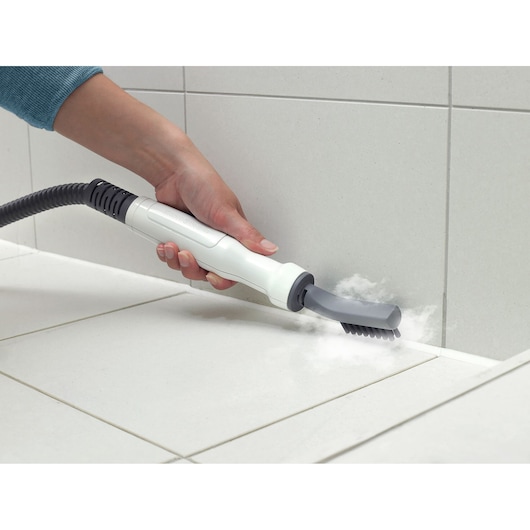 BLACKDECKER BHSM169DSM stoomreiniger mondstuk met borstel reinigt voeg op witte tegelvloer, close-up.