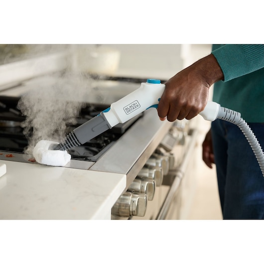 BLACK+DECKER BHSMP2008 handstoomreiniger wordt gebruikt om een kookplaat schoon te maken, zichtbare stoom.