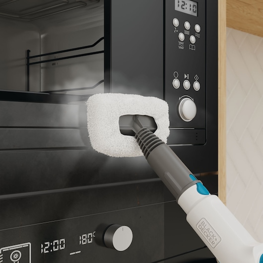 Foto van BLACK+DECKER BHSMP2314 handstoomreiniger die een zwarte ovendeur schoonmaakt met een witte pad-accessoire.