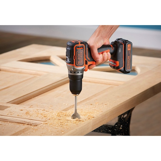 Photo d'une perceuse sans fil BLACK+DECKER BL186K1B2 en cours d'utilisation sur une porte en bois avec copeaux visibles.