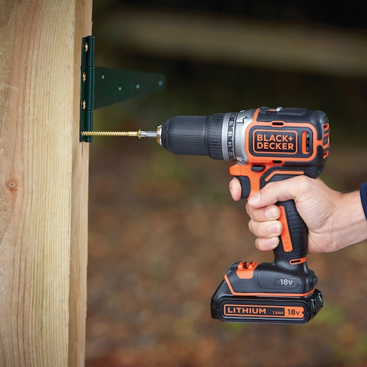 BLACKDECKER BL186K perceuse sans fil vissant une vis dans un poteau en bois, vue latérale en extérieur.
