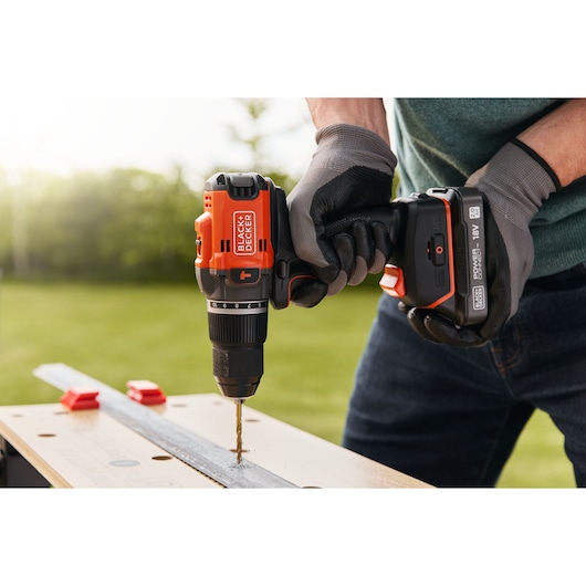Photo de la perceuse sans fil BLACKDECKER BLD683D1 en usage, perçant du métal sur un établi en extérieur.