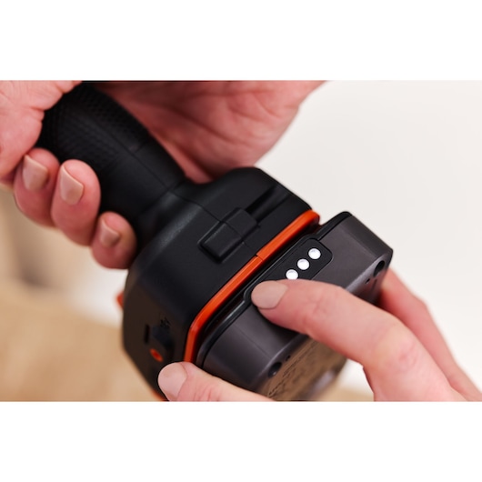 Photo rapprochée de la poignée d’outil BLACKDECKER BLD683D1 avec main appuyant sur le bouton d’indicateur de batterie, fond blanc.
