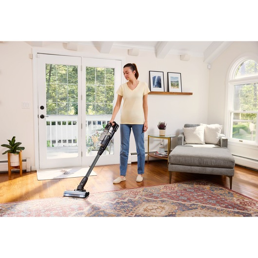 Foto van de BLACKDECKER BSV520BL2P snoerloze steelstofzuiger in gebruik op houten vloer bij vloerkleed in lichte woonkamer.