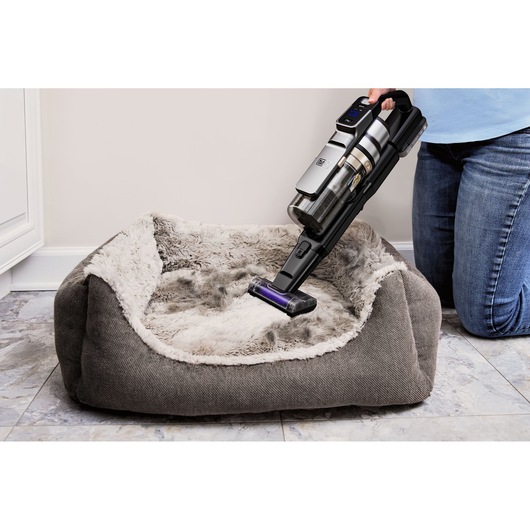 BLACKDECKER BSV520BL2P snoerloze stofzuiger reinigt een grijs pluche huisdierenbed op tegelvloer, handmodus.