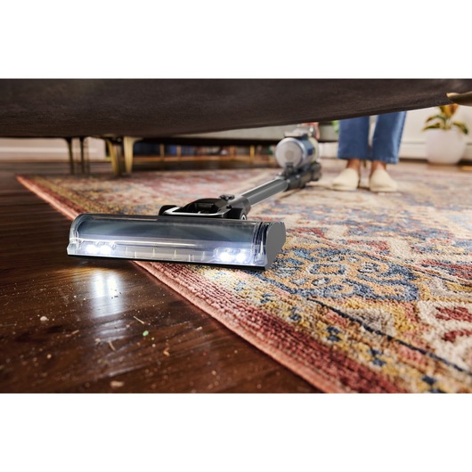 BLACKDECKER BSV520BL2P snoerloze stofzuiger reinigt onder een bank op een patroonkleed, close-up hoek.