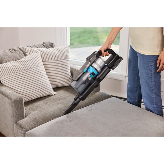 BLACKDECKER BSV520BRB stofzuiger reinigt grijze bank met gestreepte kussens in de woonkamer.