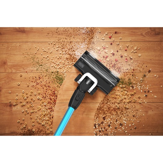 BLACKDECKER BSV520BRB draadloze stofzuiger reinigt ontbijtgranen en vuil op houten vloer, bovenaanzicht.