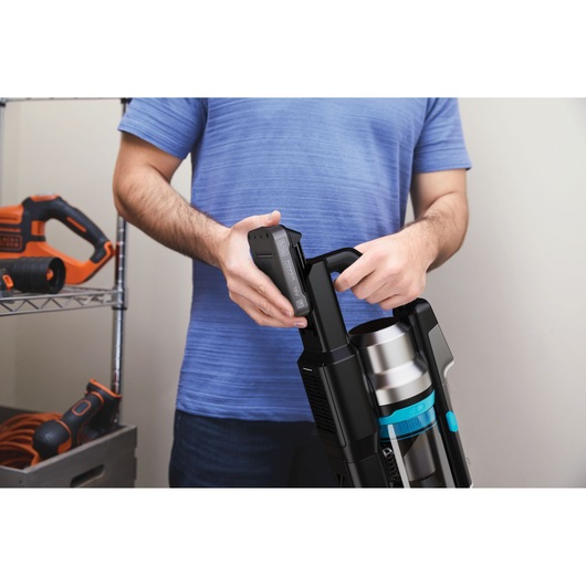 Foto van een persoon die een accu plaatst in een BLACK+DECKER BSV520BRB snoerloze stofzuiger in een garage.