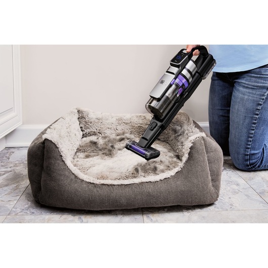 BLACKDECKER BSV520BRP handheld stofzuiger reinigt een grijs pluche dierenbed op een tegelvloer.