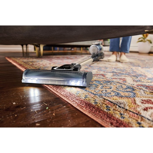 BLACKDECKER BSV525BLP snoerloze stofzuiger reinigt onder meubels op een patroonkleed en houten vloer.