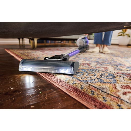 BLACKDECKER BSV525BRP snoerloze steelstofzuiger reinigt onder meubel op een patroonkleed en houten vloer, close-up.