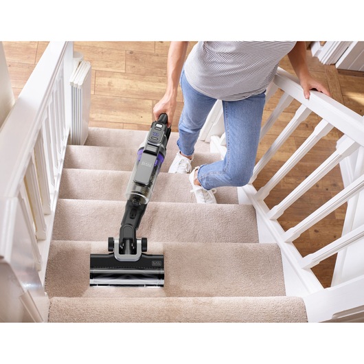 BLACKDECKER BSV525BRP snoerloze stofzuiger reinigt beige beklede trap, vastgehouden door een persoon.