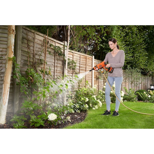 Foto van BLACK+DECKER BZOSW1 draagbare hogedrukreiniger die water op tuinplanten sproeit.