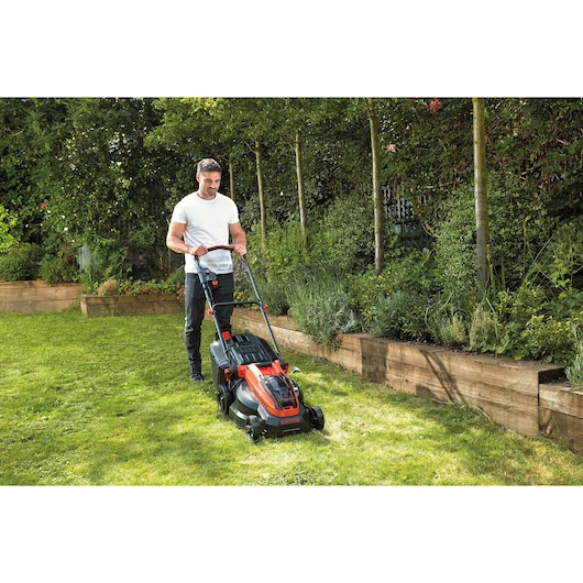BLACKDECKER CLM3825L2 tondeuse utilisée sur une pelouse de jardin près de jardinières en bois.