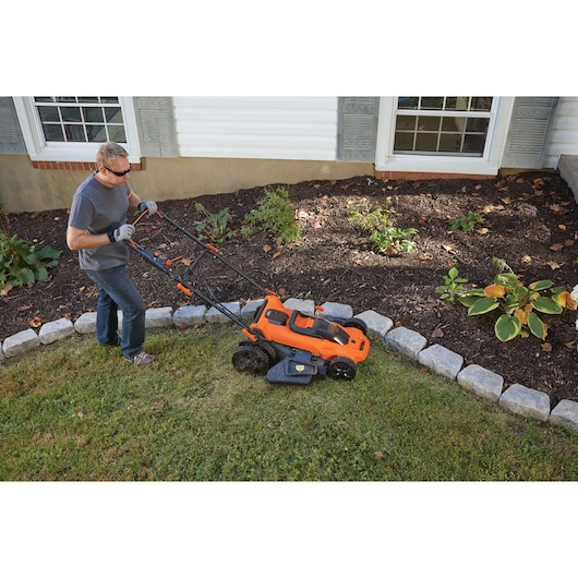 BLACKDECKER CLMA4820L2 tondeuse à gazon sans fil orange utilisée près d'un massif, vue latérale extérieure.