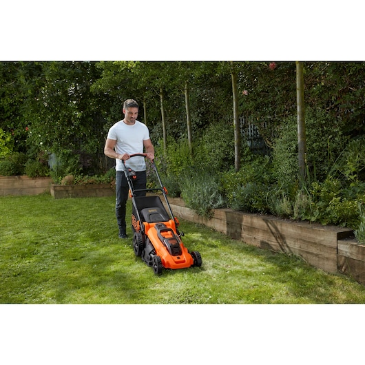 BLACKDECKER CLMA4825L2 tondeuse à gazon utilisée sur herbe près d'un massif, design orange et noir.