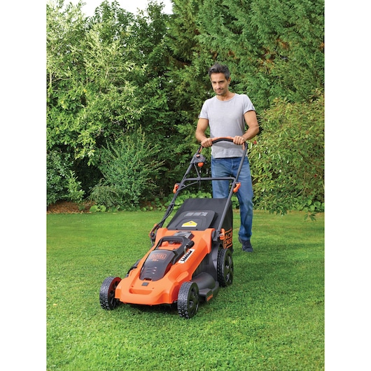 Photographie de la tondeuse BLACKDECKER CLMA4825L2 utilisée sur une pelouse, orange et noire, cadre de jardin