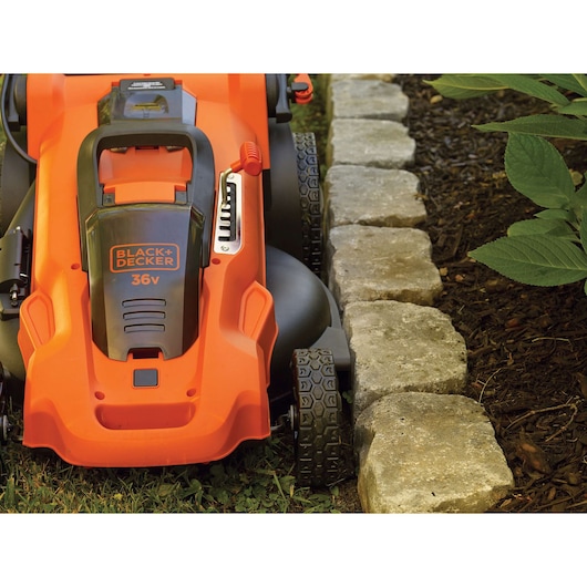 Photo de la tondeuse BLACKDECKER CLMA4825L2 en gros plan, près d'un bord en pierre, carrosserie orange, logo 36V.
