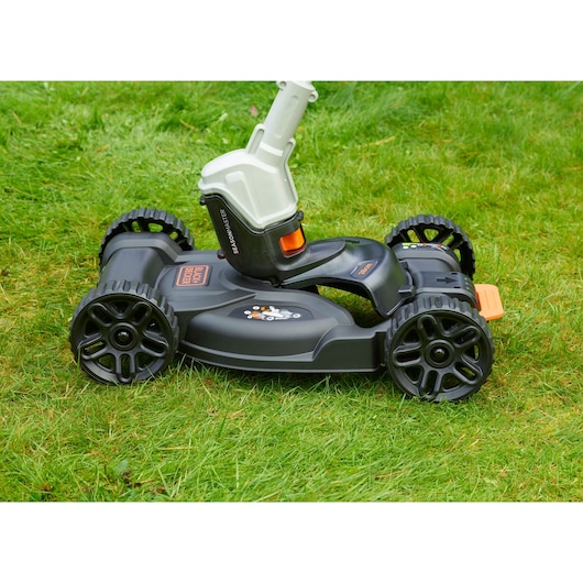 BLACK+DECKER CM100 grasmaaieraccessoire met vier zwarte wielen en zwarte behuizing, gefotografeerd op groen gras.