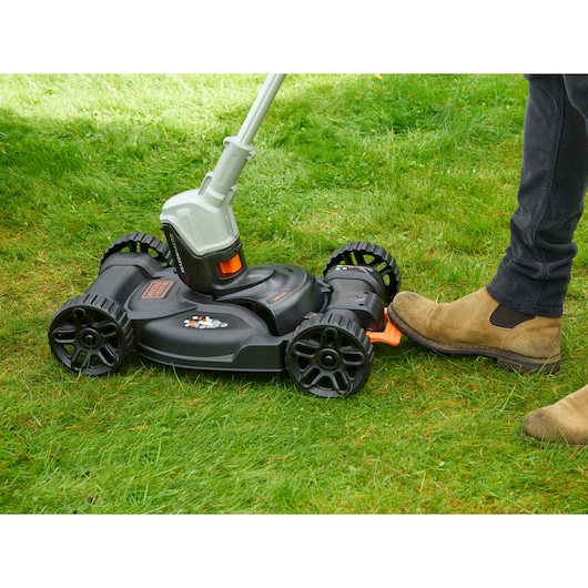 BLACKDECKER CM100 grasmaaieropzetstuk op gras, zijaanzicht, zwart en oranje ontwerp met voetpedaal.