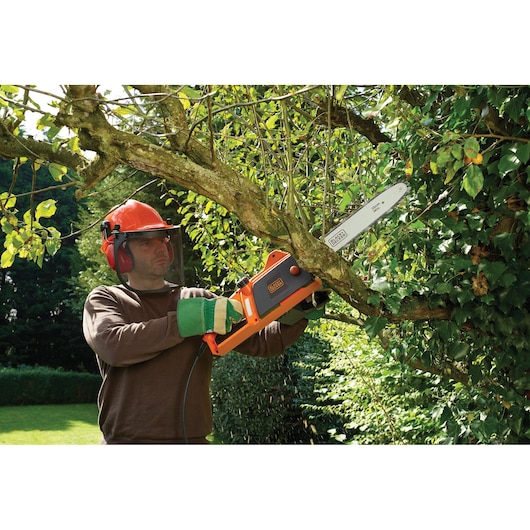 Foto van BLACKDECKER CS1835 kettingzaag die een boomtak buiten snoeit.