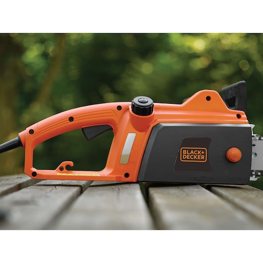 Foto van BLACK+DECKER CS1835 elektrische kettingzaag, zijaanzicht, oranje met zwarte behuizing, op houten ondergrond buiten.