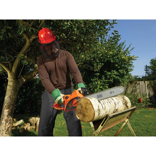 BLACKDECKER CS2040 kettingzaag zaagt hout in tuin, vastgehouden door persoon met veiligheidsuitrusting.