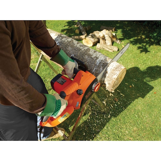 Foto van de BLACKDECKER CS2040 kettingzaag die een houtblok buiten zaagt, oranje en zwart gereedschap.