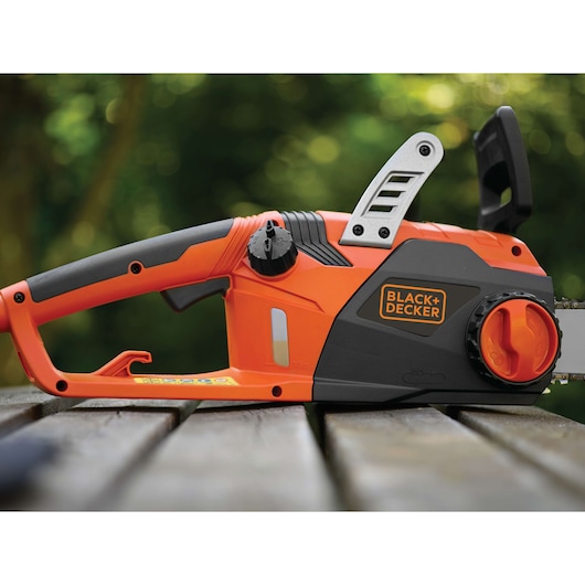 Photo de la tronçonneuse électrique BLACK+DECKER CS2245, orange et noire, vue latérale sur table en bois en extérieur.