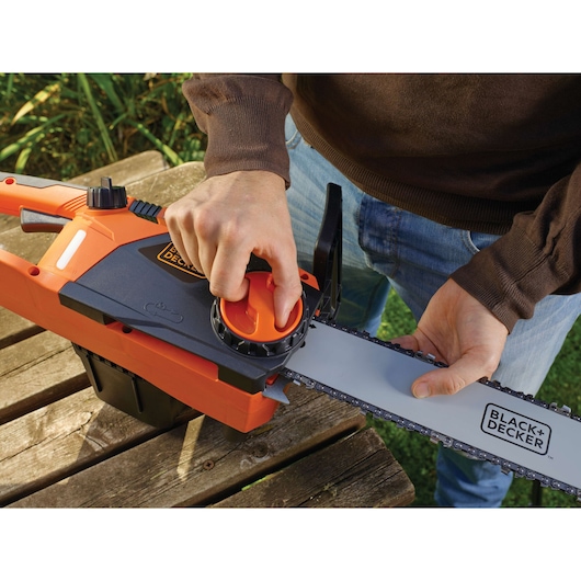 Photographie de la tronçonneuse BLACK+DECKER CS2245 réglée à la main, avec vue sur le bouton de tension de chaîne et la lame.