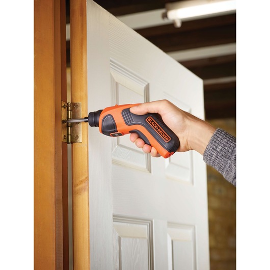 BLACK+DECKER CS3651LC oranje draadloze schroevendraaier gebruikt op een deur scharnier.