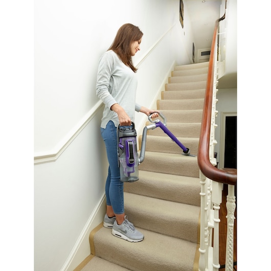 Aspirateur BLACKDECKER CUA625BHP avec des accents violets utilisé sur des escaliers en tapis.