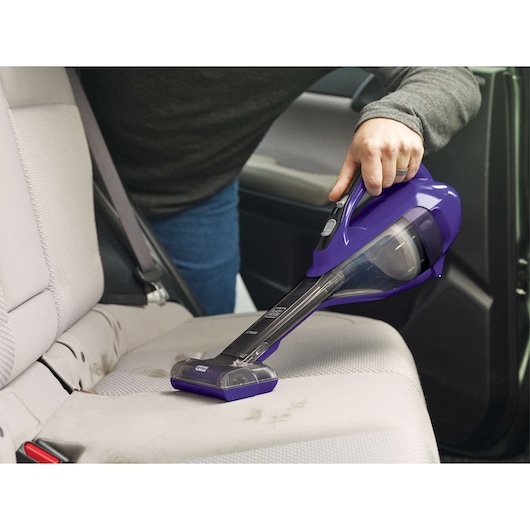 Paarse BLACK+DECKER DVA325JP07 handstofzuiger gebruikt om een autostoel te reinigen, zijkant.